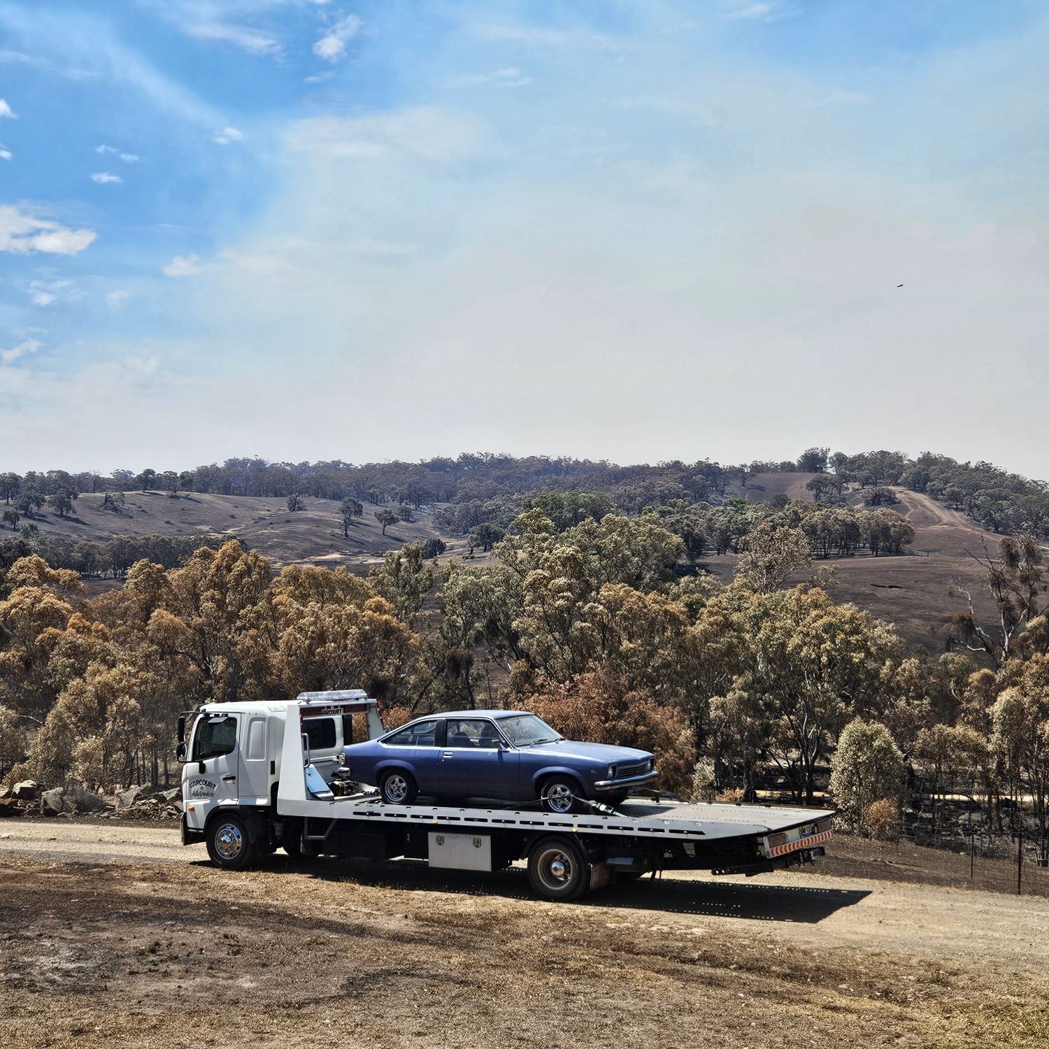 Harcourt Auto Wreckers tilt tray carrying a Holden Torana through the Victorian bush